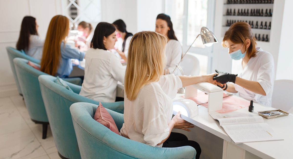 Group of girlfriends relax on manicure procedure in beauty salon. Professional beautician and female customers, nail care in spa, fingernail treatment
